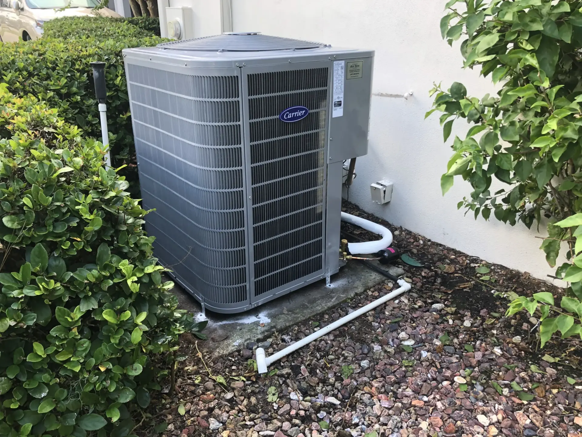 Air conditioning unit by Carrier installed outside, surrounded by greenery and gravel, relevant to HVAC services and installation in Central Florida.
